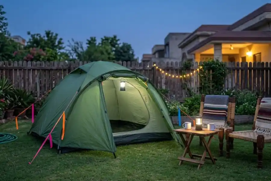 Garden camping setup with a green dome tent, camp chairs, and string lights in a backyard at dusk